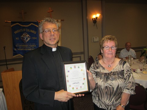 Jane Ferguson, President of the St. Thomas Aquinas CWL, presents Father Michael with a plaque on Behalf of MP Rick Dykstra from the Government of Canada